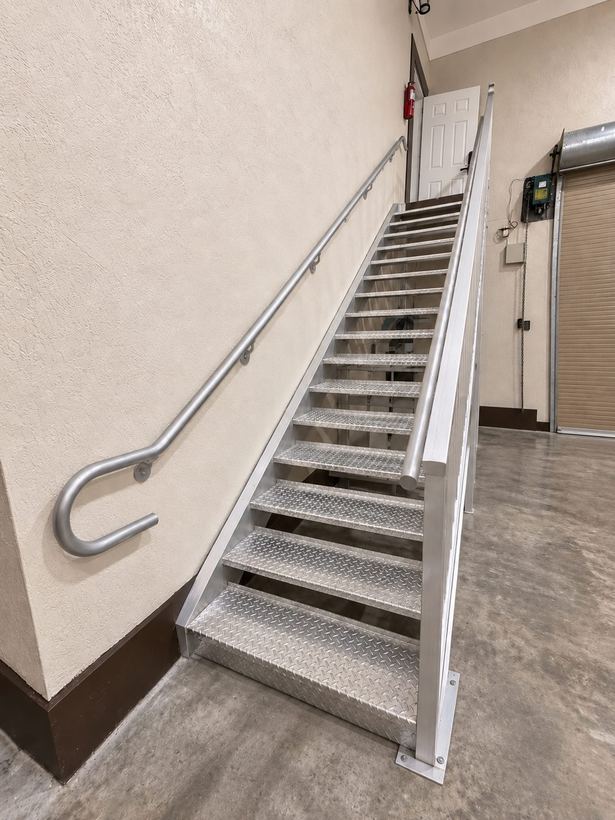 Aluminum commercial staircase with diamond-plate treads and a return handrail